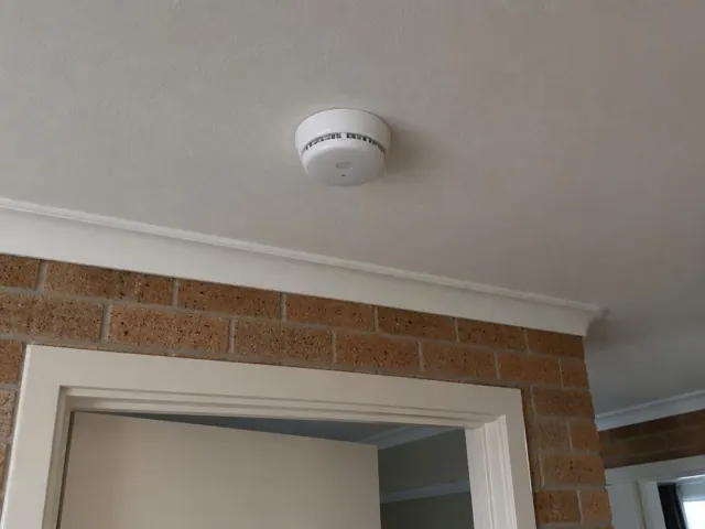 Ceiling smoke alarm above a brick interior wall and doorway in Belmont